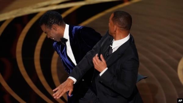 FILE - Will Smith, right, hits presenter Chris Rock on stage at the Oscars, March 27, 2022, at the Dolby Theatre in Los Angeles.