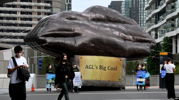 Morning commuters walk past a giant inflatable depicting a piece of coal erected by Greenpeace outside Australian energy company AGL in Melbourne on March 28, 2022. 