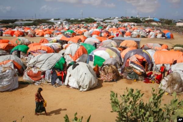 FILE - Somalis who fled drought-stricken areas walk next to a cluster of makeshift shelters at a camp for the displaced on the outskirts of Mogadishu, Somalia, June 4, 2022.