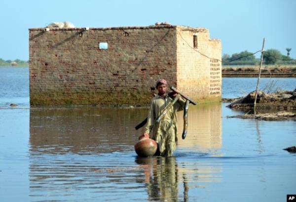 FILE - A man carries some belo<em></em>ngings as he wades through floodwaters in Jaffarabad, a flood-hit district of Baluchistan province, Pakistan, Sept. 19, 2022.