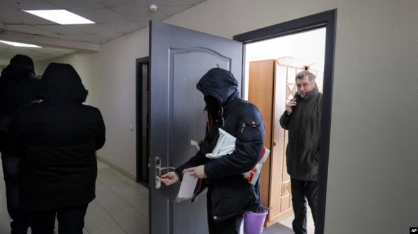 FILE - Police carry materials from the office of the Belarusian Association of Journalists as Andrei Bastunets, the group's leader, watches, in Minsk, Feb. 16, 2021. The association said Oct. 27, 2002, that journalist Ales Lyubyanchuk had been sentenced to three years in prison.